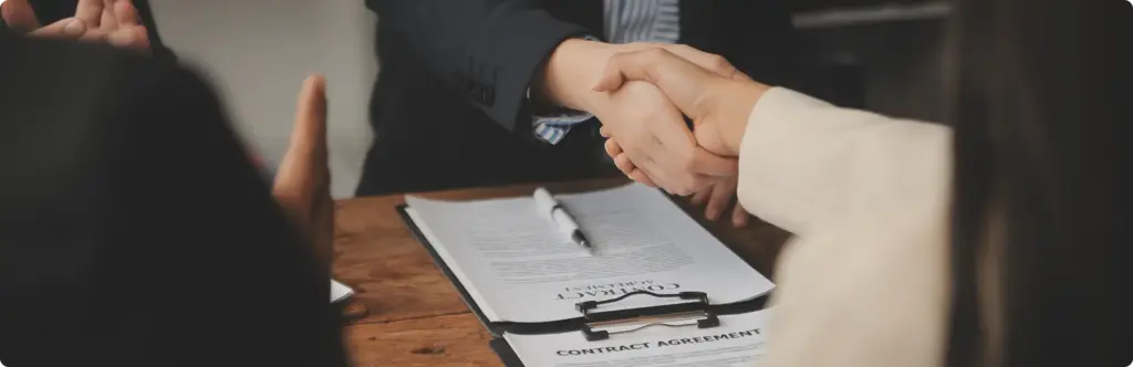 Partnerzy biznesowi ściskają sobie dłonie nad stołem z umową i dokumentami podczas spotkania biznesowego.