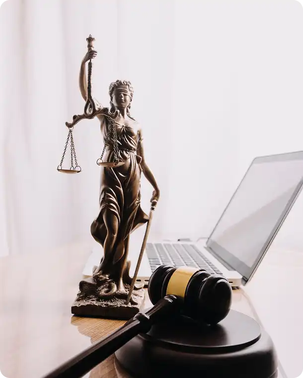 Statua Temidy i młotek sędziowski na stole obok laptopa.